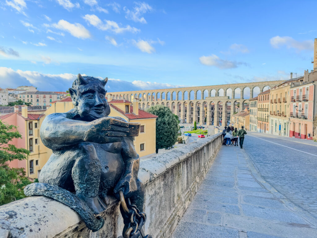 statue of devil with roman aqueduct in background in Segovia, spain