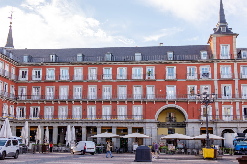 corner of plaza mayor madrid with people walking around and umbrella over cafe tables